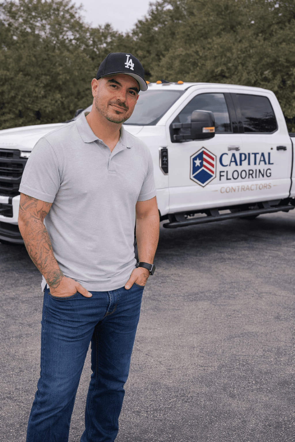 Man in grey polo and LA cap standing before a white Capital Flooring truck.